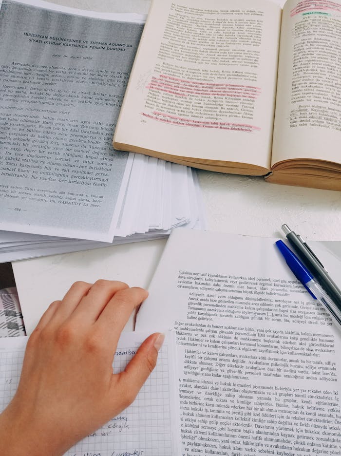 Open books and notes on a desk, featuring a hand studying, symbolizing academic focus.