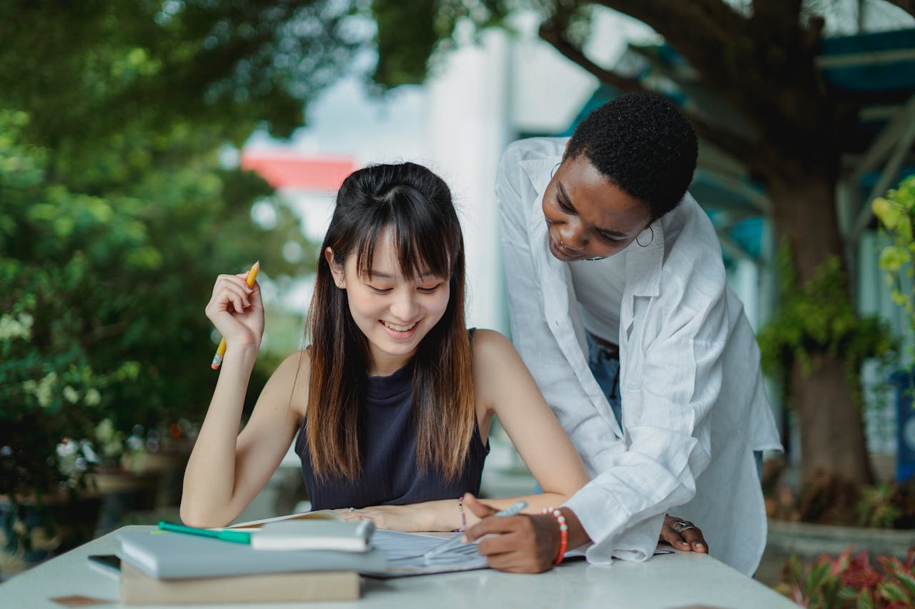 Two diverse students collaborate on homework outdoors, enjoying a summer day in the park.
